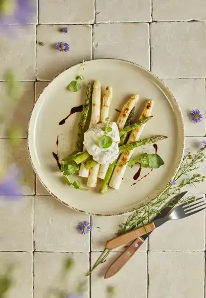 Een bord met groene en witte asperges met burrata afgetopt met balsamico.