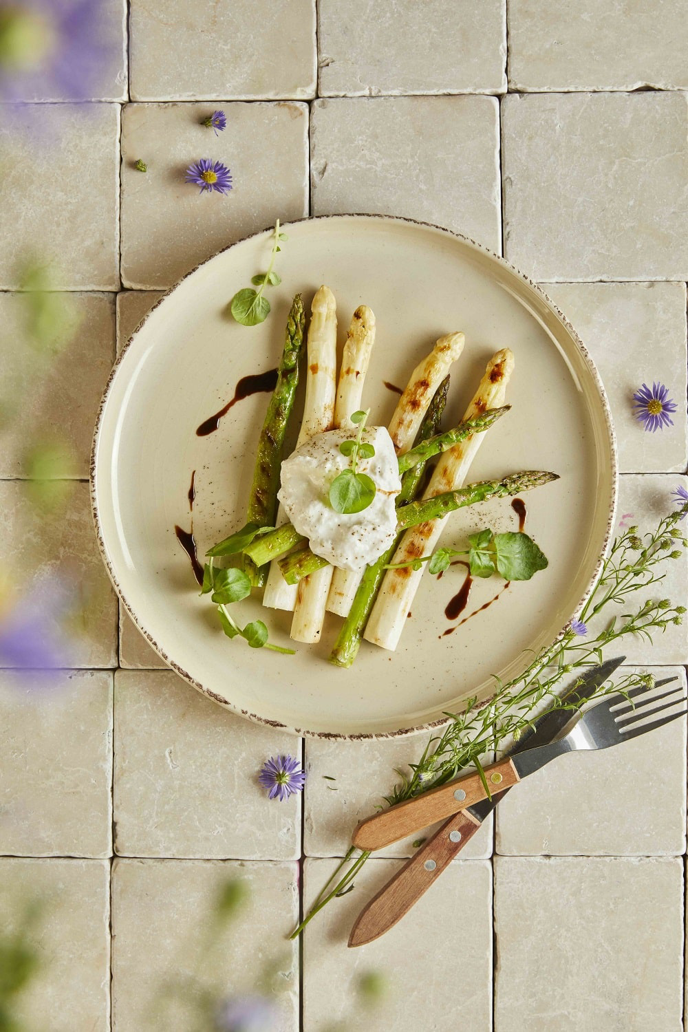 Ekoplaza-biologisch-LekkerWeten-Lente2024-asperges-burrata Een bord met groene en witte asperges met burrata afgetopt met balsamico.