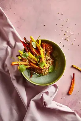 Ekoplaza-biologisch-LekkerWeten-Winter2023-regenboogwaspeendukkah Een gerecht met regenboog waspeen en zoete aardappelcrème op een roze achtergrond